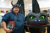 Robot artist Paul Aitken stands next to his robot dragon, a black creature with large green eyes and glowing nostrils.