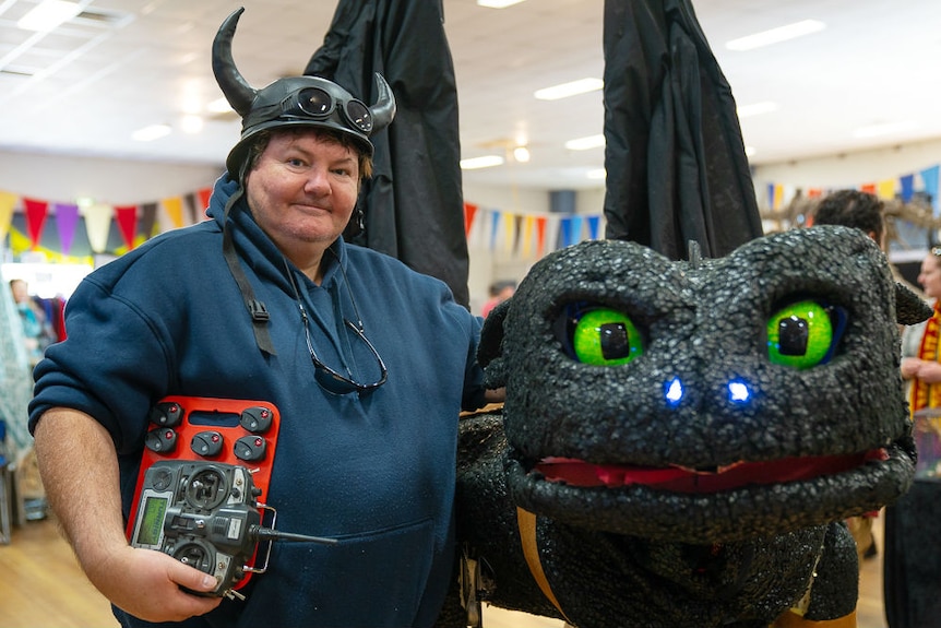 Robot artist Paul Aitken stands next to his robot dragon, a black creature with large green eyes and glowing nostrils.