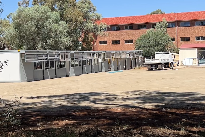 A line of demountable buildings under construction on a slab of concrete next to a school