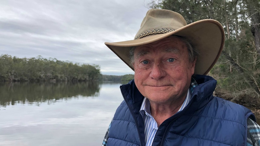 A man in a brown hat standing by a river.