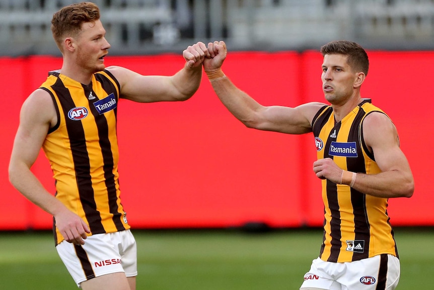 Two Hawthorn AFL players bump wrists as they celebrate a goal against Carlton in Perth.