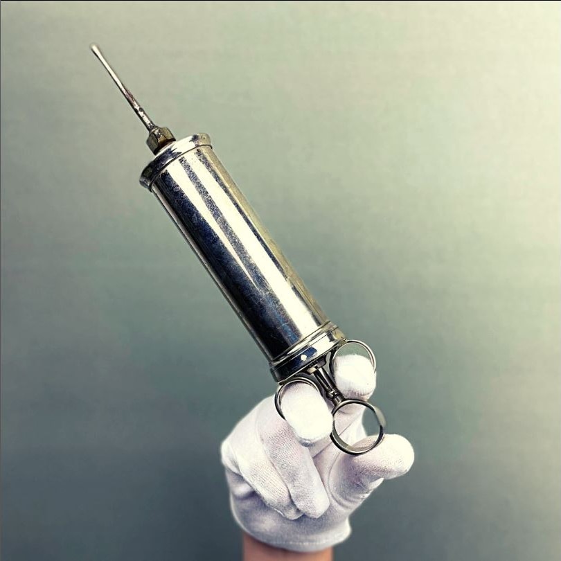 A white-gloved hand holding an old stainless steel needle