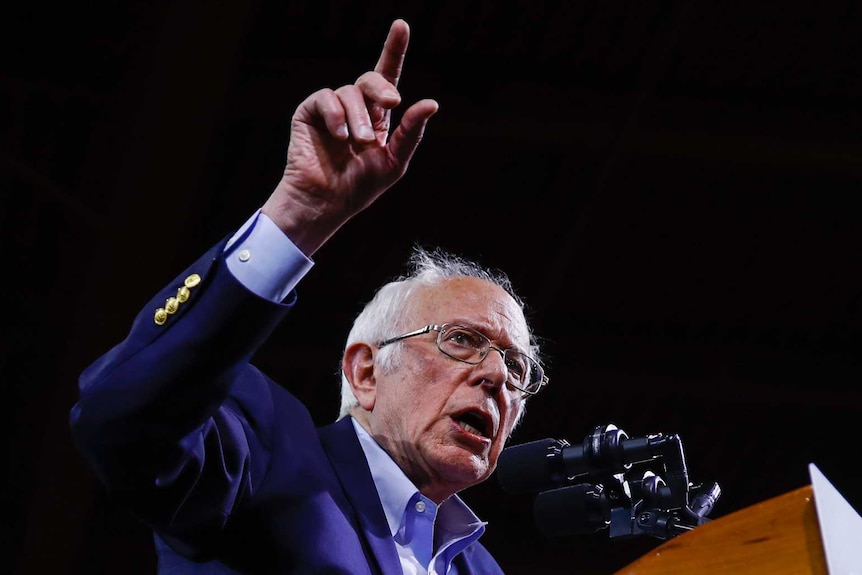 Bernie Sanders behind a podium with his arm up