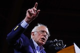 Bernie Sanders behind a podium with his arm up