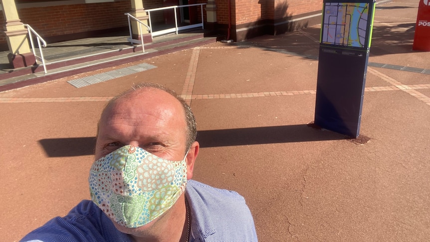 Man wearing a mask, made of fabric, in front of an old red brick building