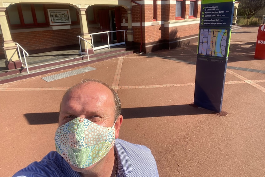 Man wearing a mask, made of fabric, in front of an old red brick building