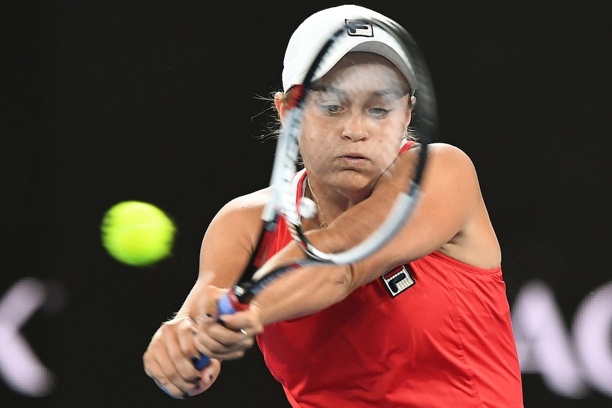 tennis player ash barty swings a racket at a moving tennis ball, her face looks like she is breathing heavily