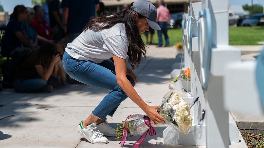 A woman wearing a baseball cap, T-shirt and jeans places flowers against a memorial.