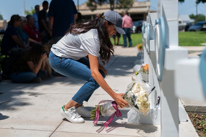 A woman wearing a baseball cap, T-shirt and jeans places flowers against a memorial.