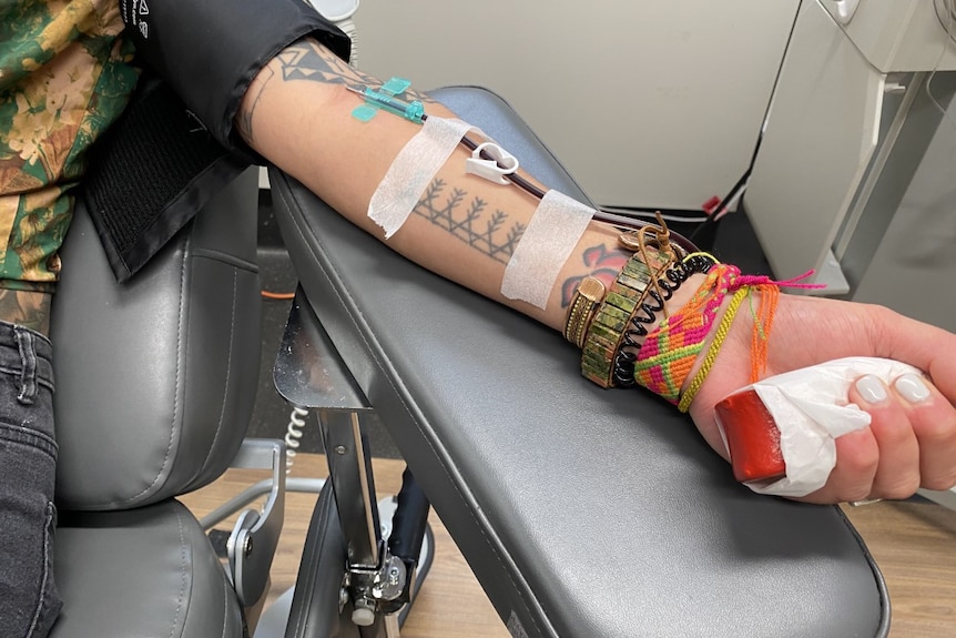 A person with tattoos on their arm is giving a plasma donation