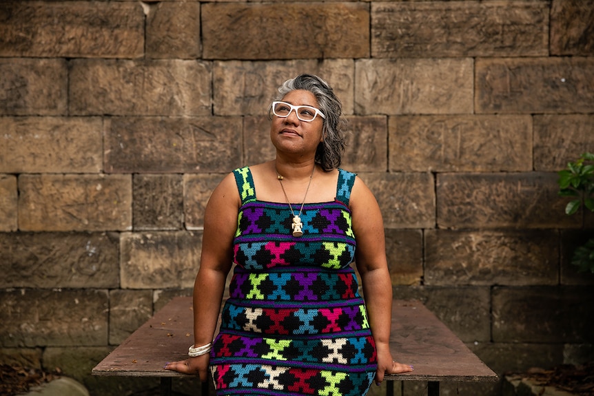 Colour photo of artist Latai Taumoepeau posing in front of sandstone background at the National Art School in Sydney.