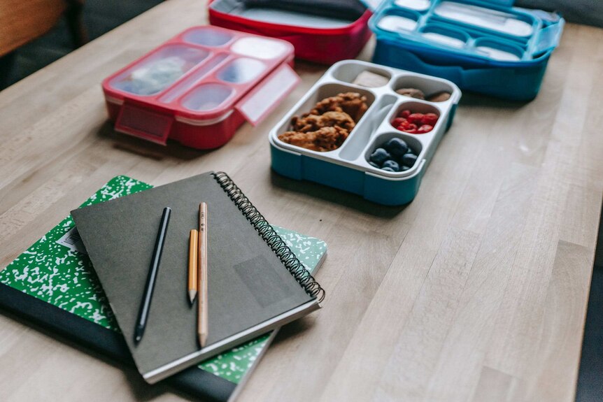 Lunch boxes and school books on a table.