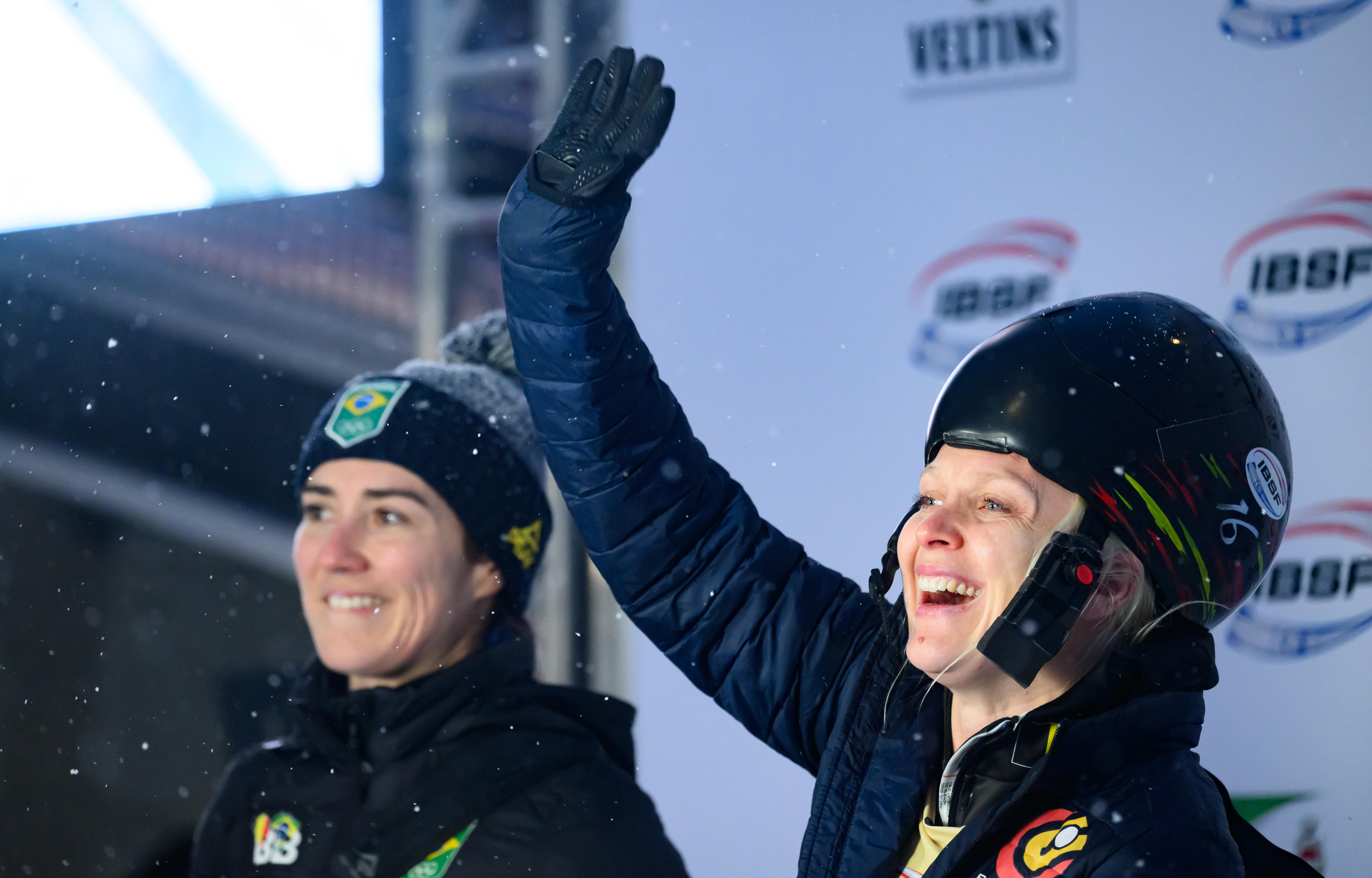 Duas mulheres em capacetes sorriem e acenam