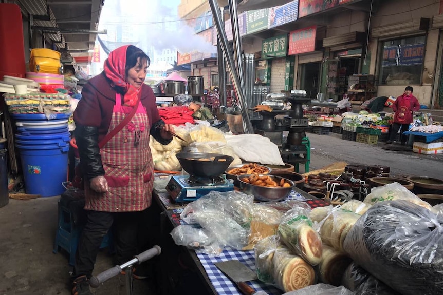 A woman all rugged up at a market standing next to a wok