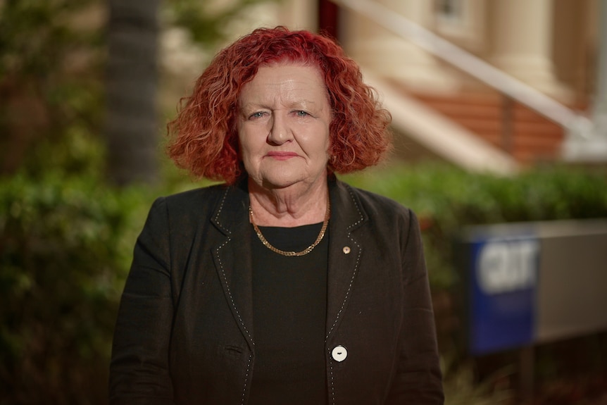 a woman in a balck jacket and top, with red curly hair