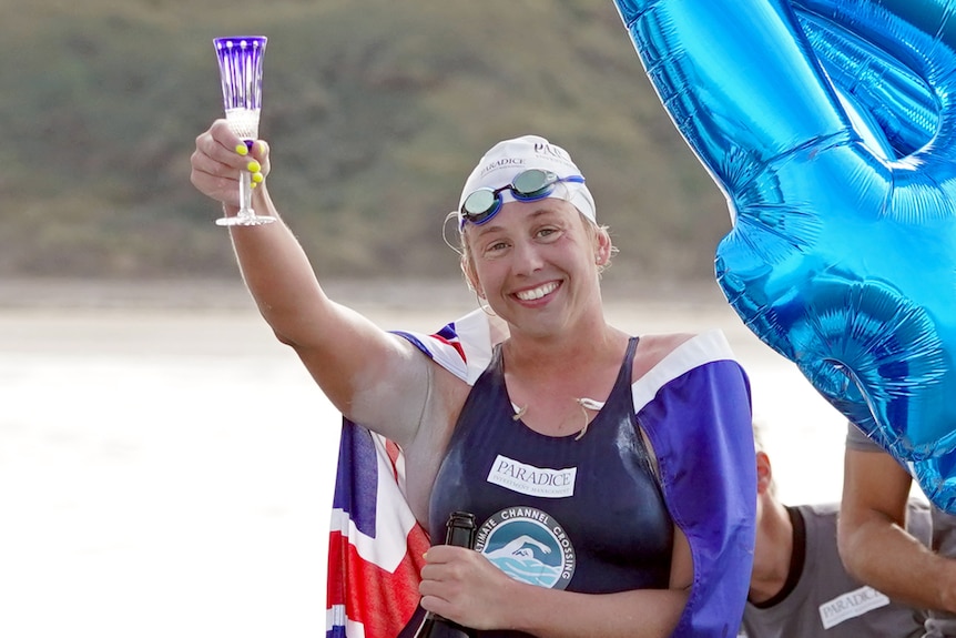Chloe McCardel raises a blue-tinted champagne flute while wearing a swimming hat and goggles