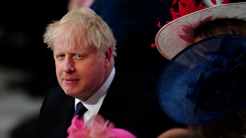 Boris Johnson looking pensive surrounded by women in hats 