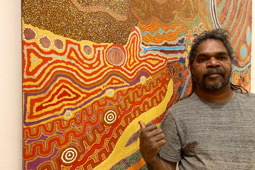 A man stands beside an elaborately patterned and colourful painting