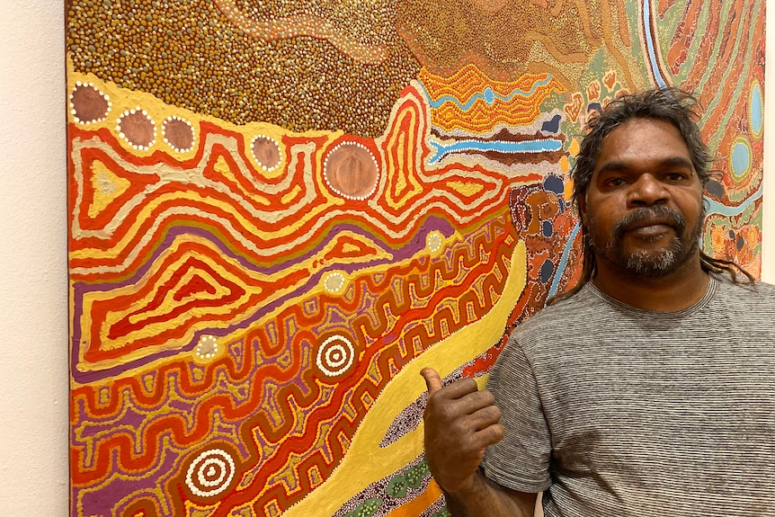 A man stands beside an elaborately patterned and colourful painting