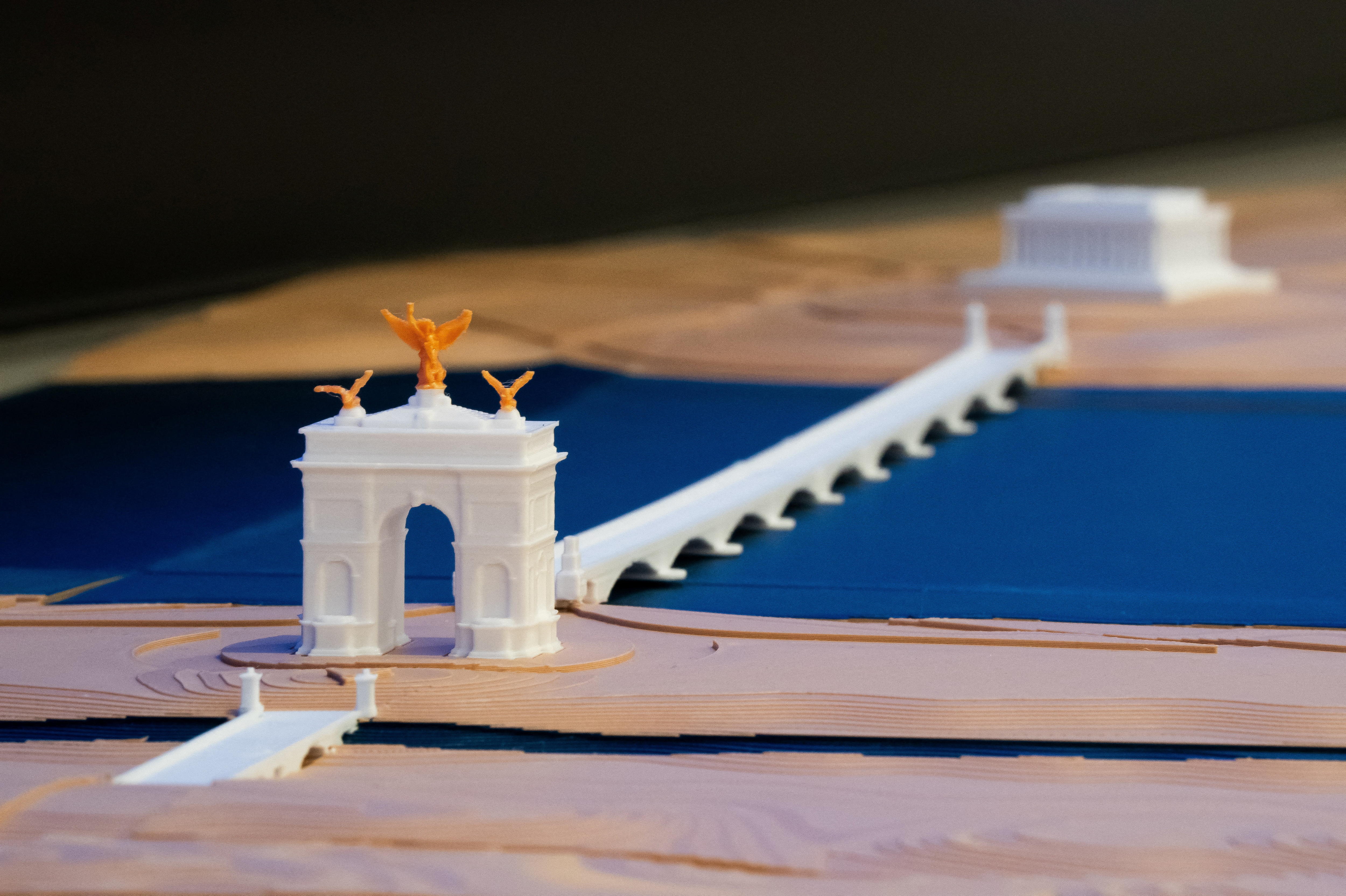 A white plastic model of an arch opposite a columned building, with a bridge between.