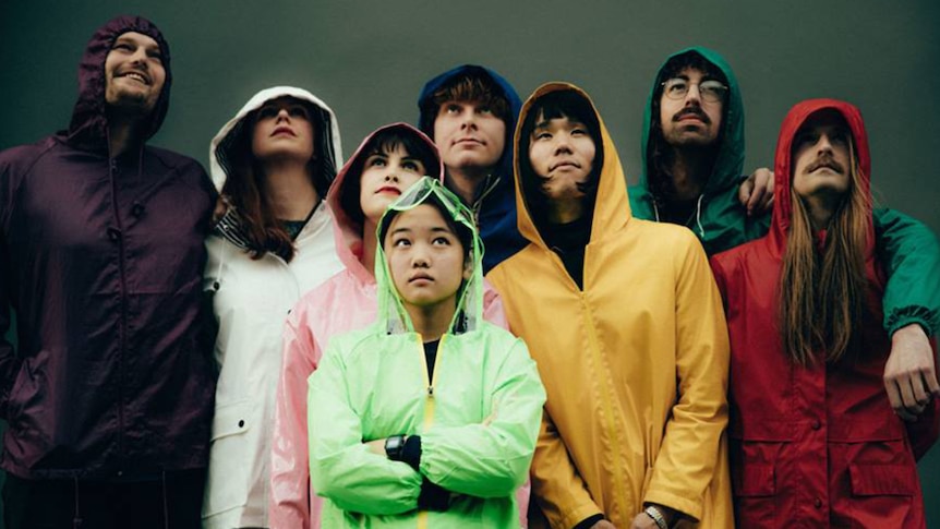 The band Superorganism stand together in multi-coloured raincoats