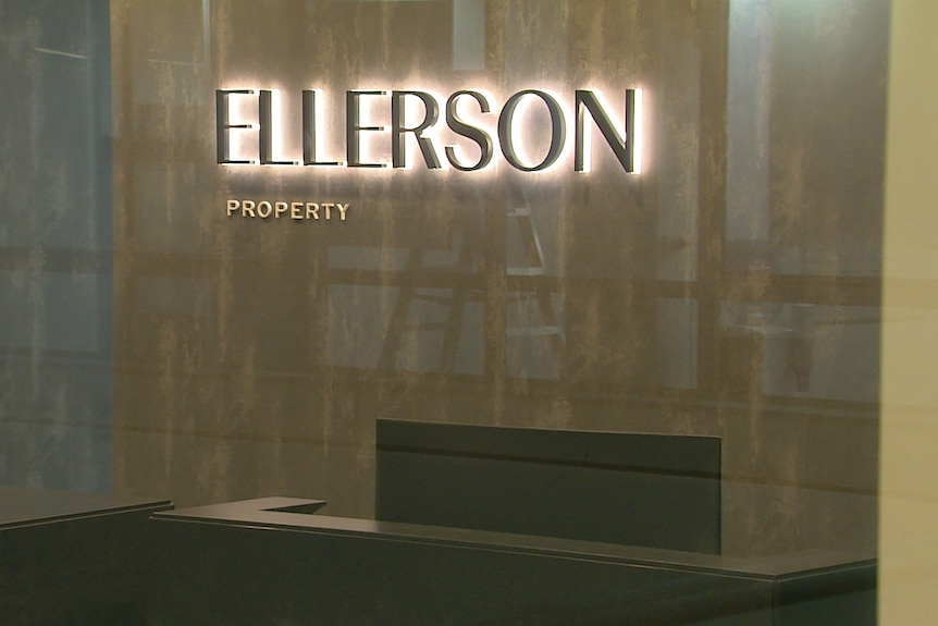 A wall with a lit sign with the words Ellerson Property, seen through a glass window.