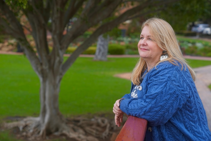 A woman leans on a bridge overlooking a lake