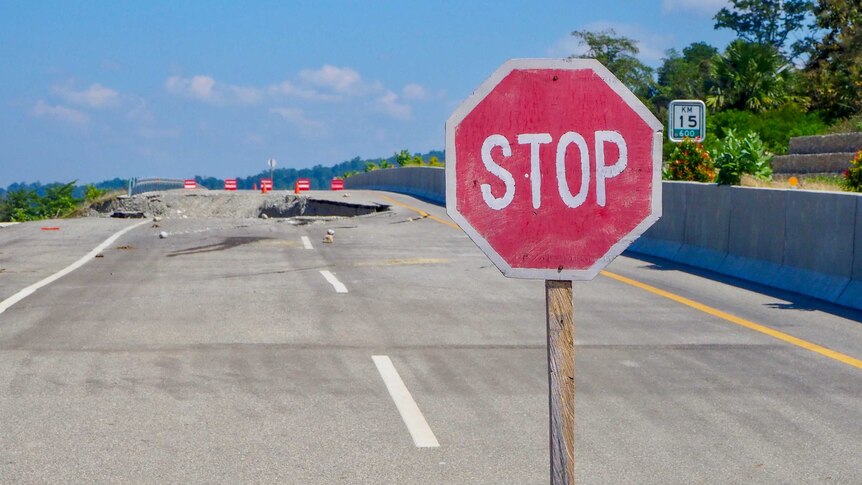A stop sign in front of a ruined road