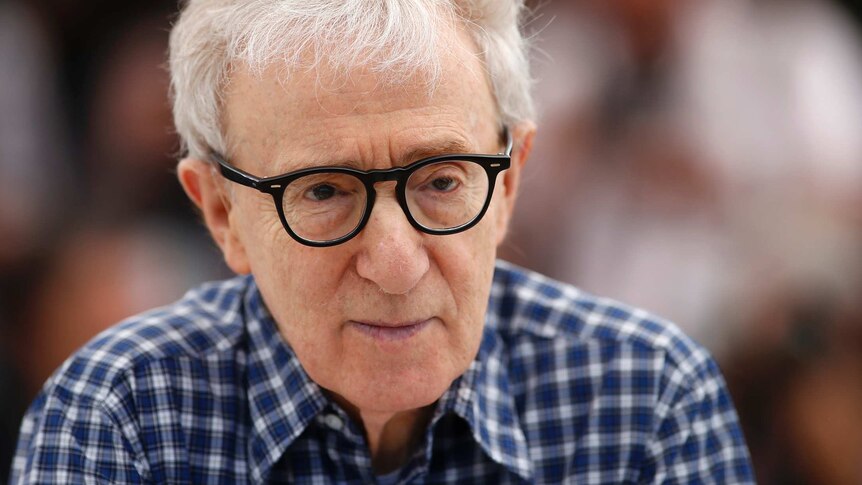 Director Woody Allen, wearing thick-framed black glasses, looks off camera with a small smile.