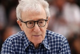 Director Woody Allen, wearing thick-framed black glasses, looks off camera with a small smile.
