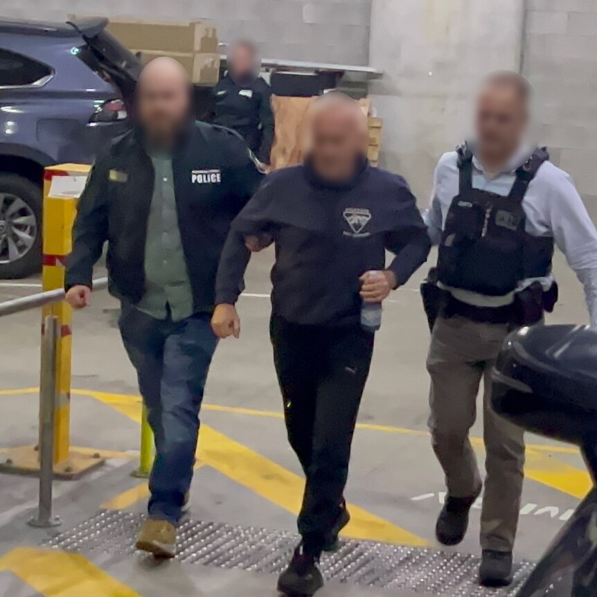 A man with a blurred face is led up a path by two other men with blurred faces.