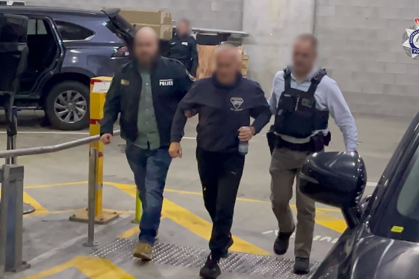 A man with a blurred face is led up a path by two other men with blurred faces.