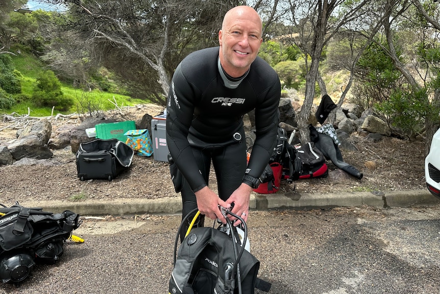 A bald man smiles in a scuba diving suit.