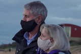 A man and woman both wear face masks on a beach