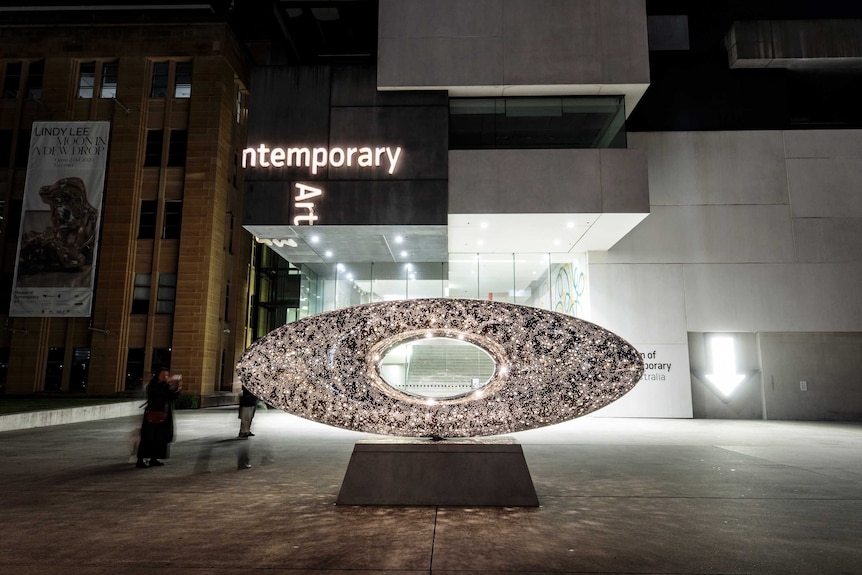 luminescent oval sculpture with hole in the centre outside the museum of contemporary art at night time