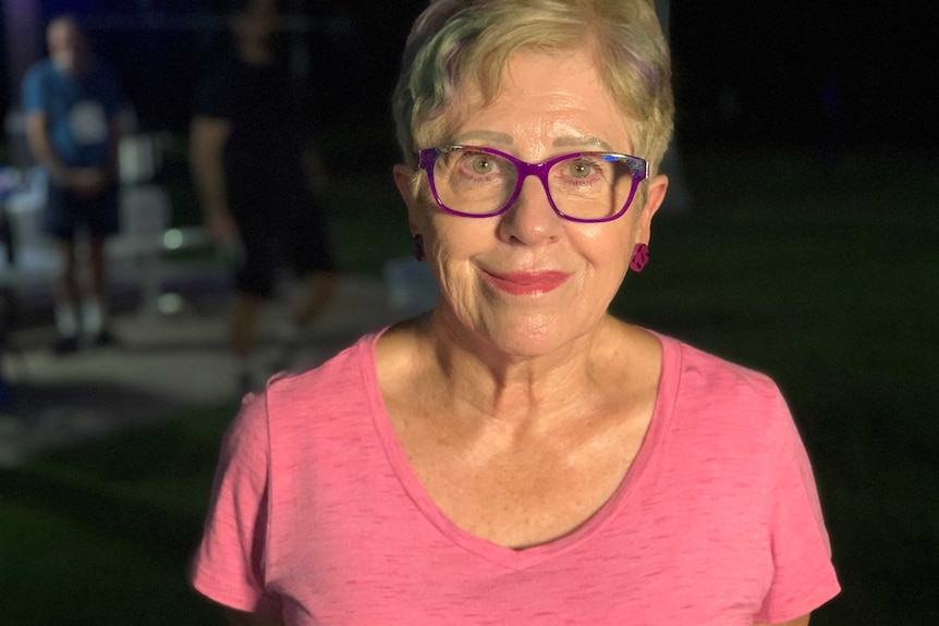 woman with purple-rimmed glasses and pick top looking at camera with a pre-dawn background