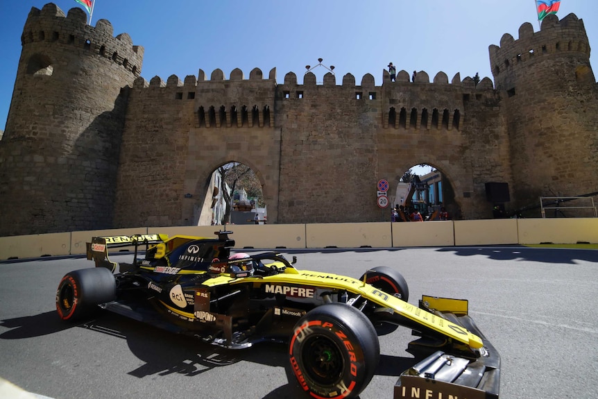 Daniel Ricciardo drives his black and yellow renault formula one car around the Azerbaijan circuit past a castle