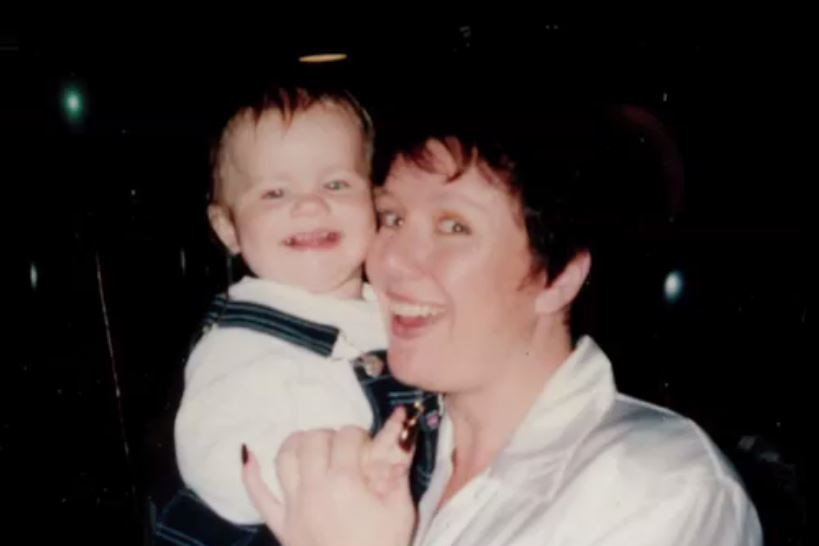 An old photograph of a woman with dark hair holding a baby, both smiling.