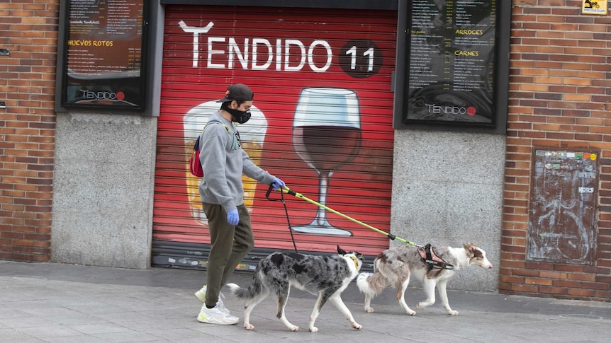 A man walks his dogs past a closed bar in Madrid
