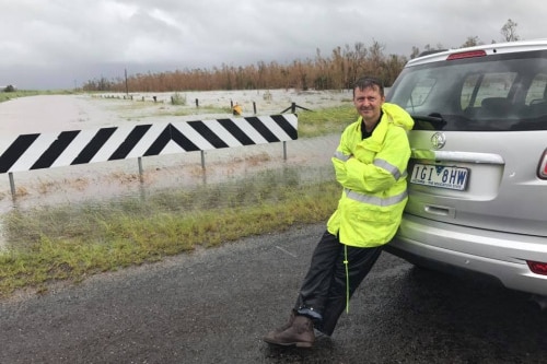 Camera operator Steve Cavenagh wears high-vis as he takes a break beside the flooded Bruce Highway