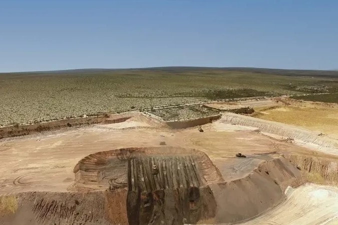 Aerial view of large mining sand pile in a pit, surrounded by scrub. 