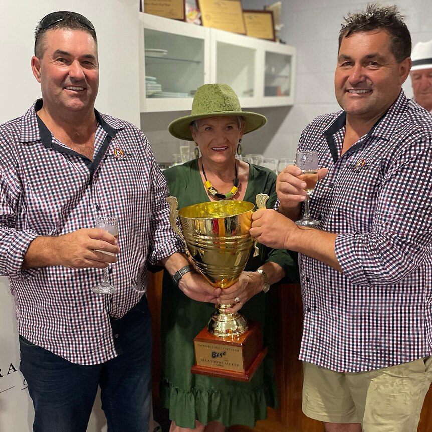 Barbara with her two sons holding a large gold trophy. 