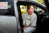 A woman with a solemn expression sitting in a car.