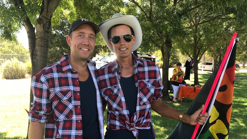 Two men in shorts and check shirts wear hats and smiles.