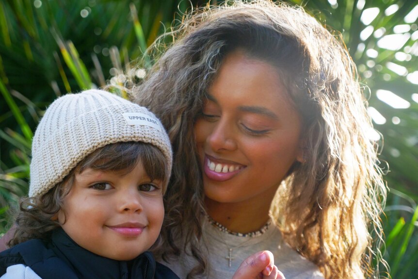 A woman with curly hair smiling at a young boy in a beanie hat.