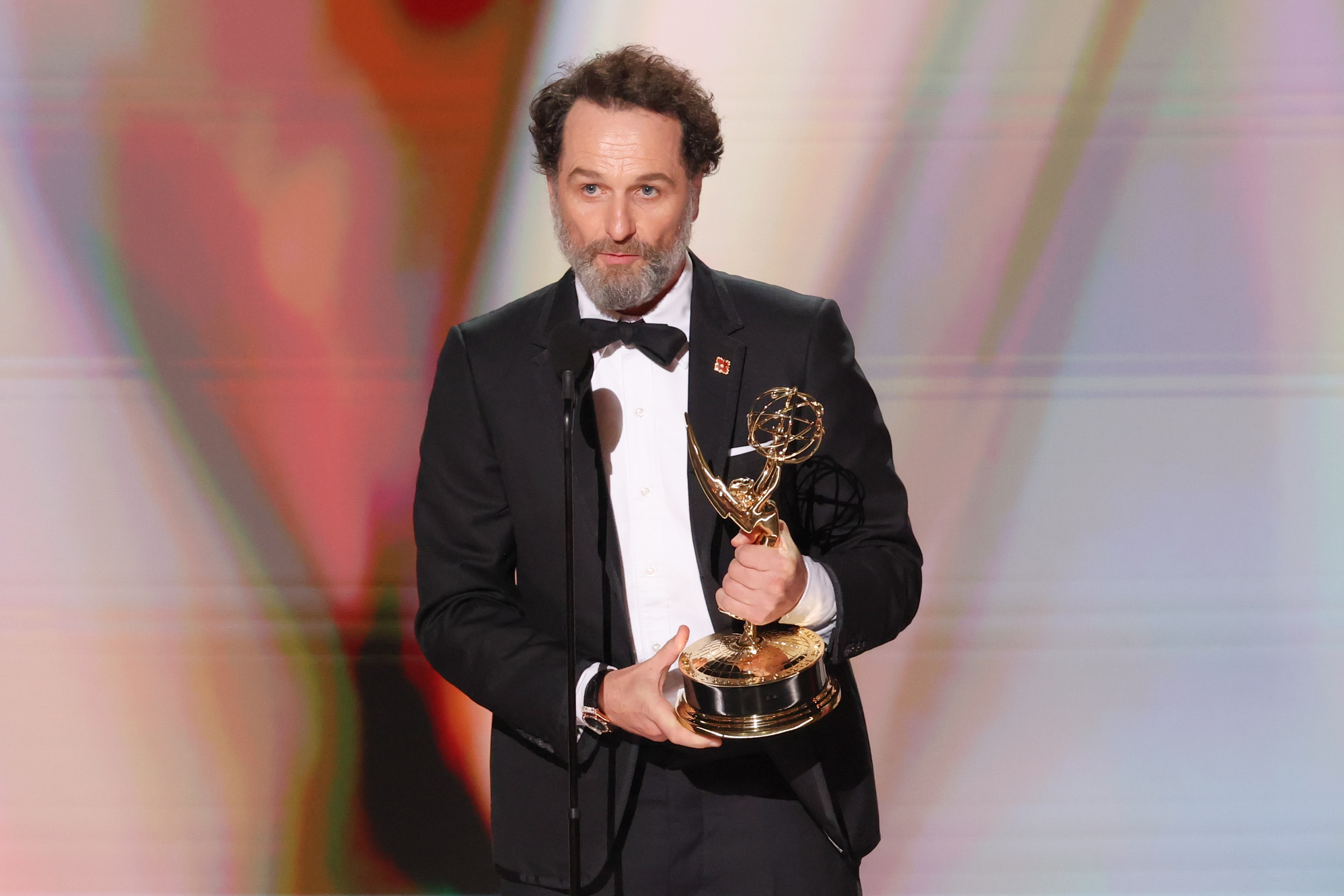 Widow's Bay star Matthew Rhys holds his Emmy on stage