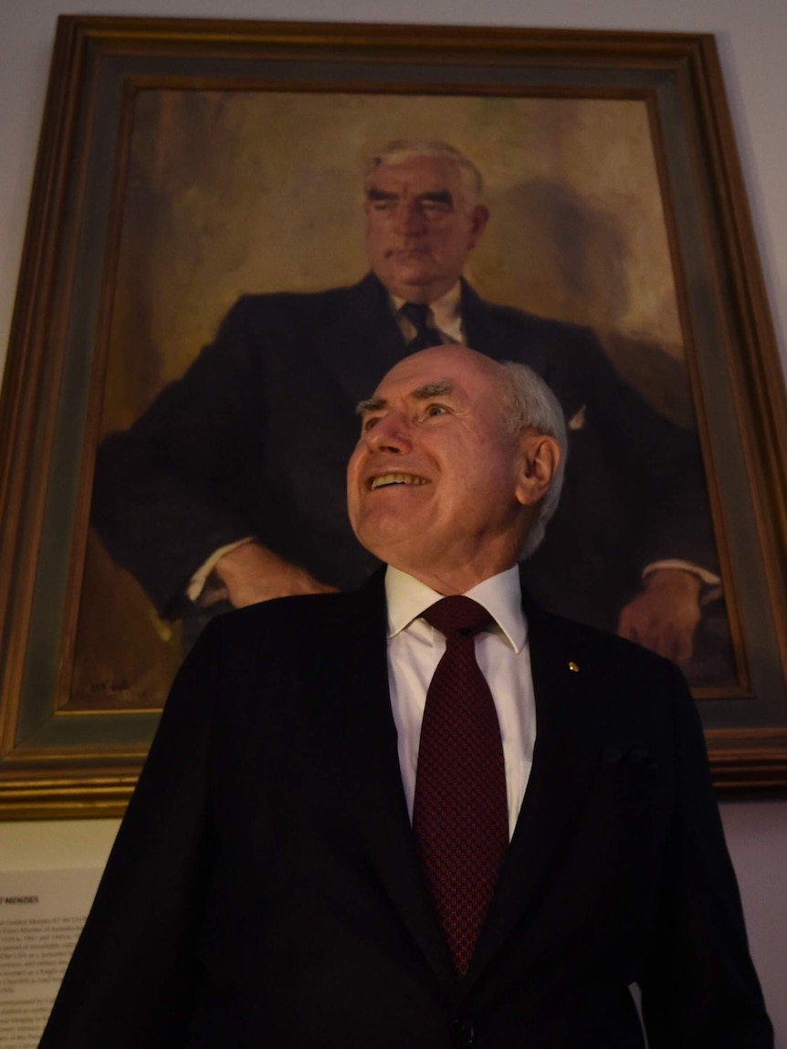 John Howard smiles as he stands in front of a portrait of Robert Menzies.