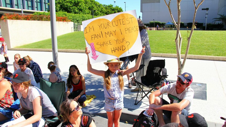 A young fan waits with a sign for the royal couple