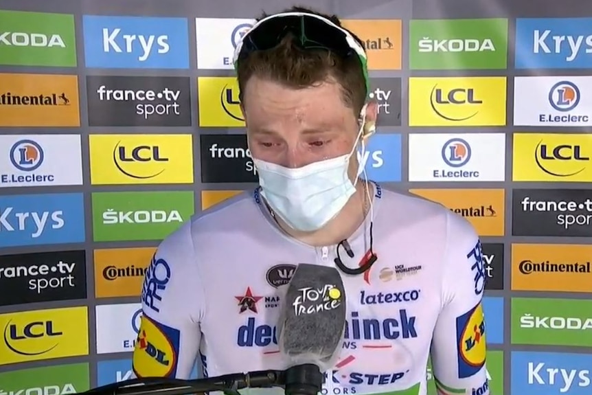 Sam Bennett, wearing white lycra and a white surgical mask cries during an interview.