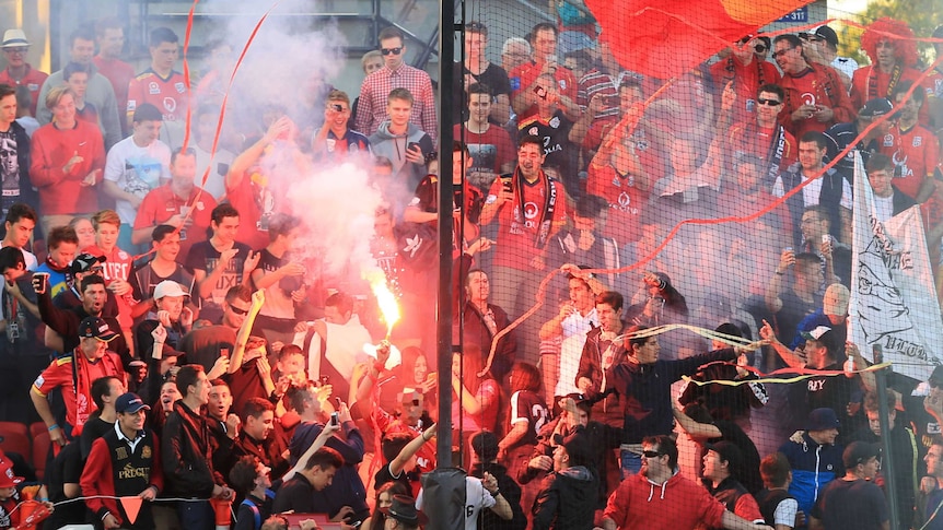 Soccer fans stand around a flare in the grandstands.